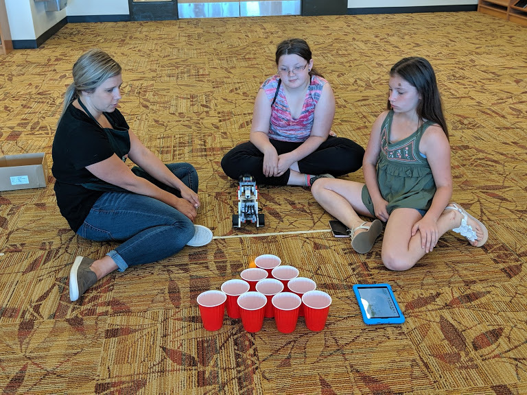 Lead teacher at Snapology of Lancaster Emily Puwalski, Karrissa McCauley, and Nevaeh Seiders code a robot to toss a ball into a cup in Snapology at Creator Camp.